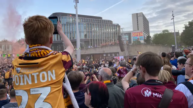 Boy wearing Bradford top with Pointon 23 on back takes photo over fans of players