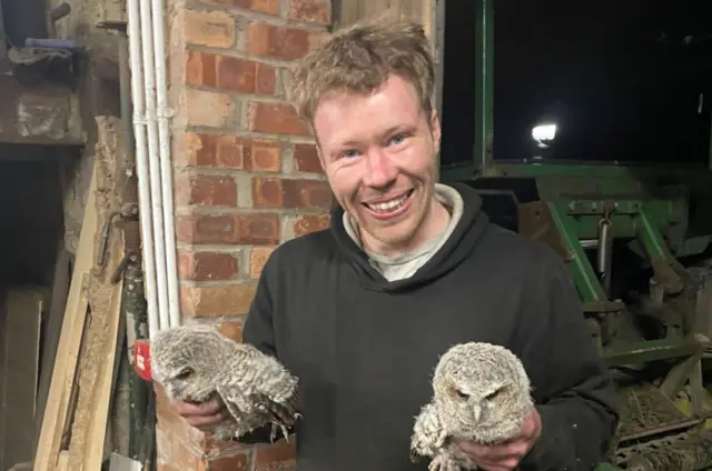 Adam Carruthers holding some owls with tools and wood visible in the background