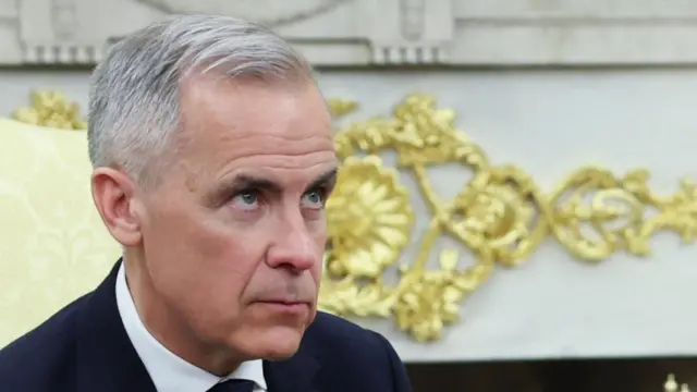 A close up of Carney who is looking up as reporters ask questions
