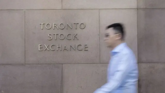 Blurred man in light blue shirt walks past a wall marked with the wording Toronto Stock Exchange
