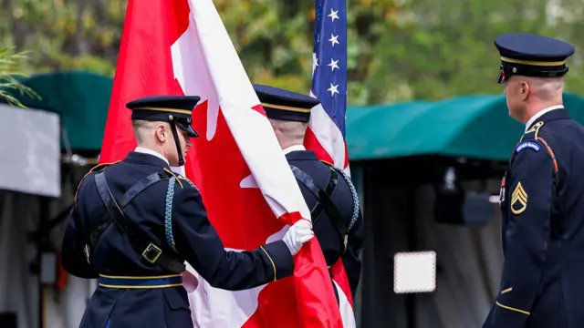 Two guards propping up a Canadian and US flag respectively