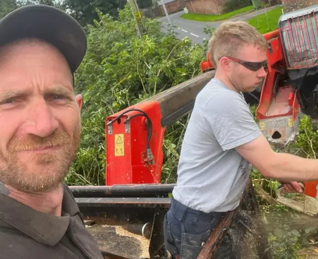 Mr Graham takes a selfie as Mr Carruthers cuts a tree with a chainsaw