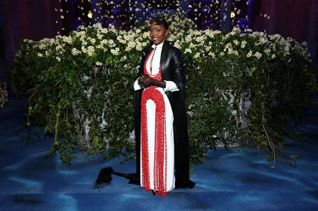 Edebiri is wearing a black weather overall over a white dress bejewelled with red coral beads
