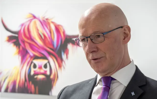 John Swinney stands in front of a picture
