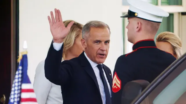 Mark Carney in black suit, white shirt and black tie waves to the press as he enters his car under the White House entrance portico, a member of the US military stands in uniform with his back to the passenger door