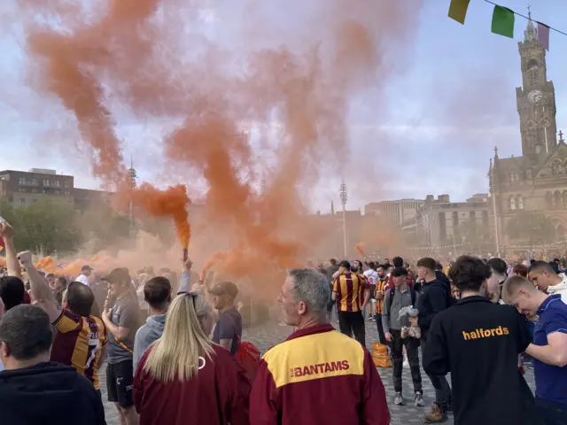 Numerous Bradford fans beneath orange smoke from a flare