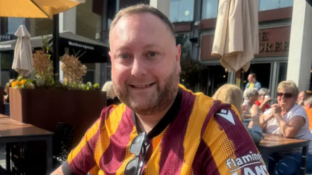 Robert Cranmer wearing a Bradford City top outside in a beer garden smiling