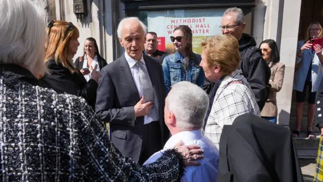 Sir Brian Langstaff at the centre of the image, he is surrounded by victims and campaigners outside Central Hall in Westminster