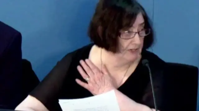 Mary Grindley wears a black top and has one hand on her chest