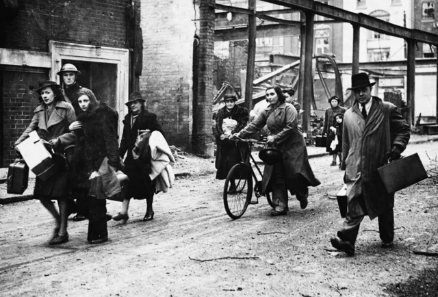 Black and white image of Southampton residents walking along a bomb-damaged street