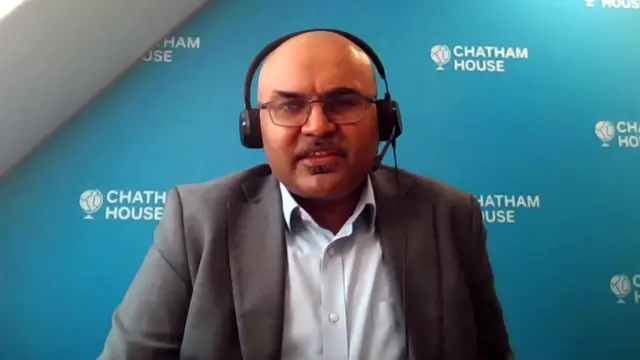 Chietigj Bajpaee in a suit against a blue background featuring the Chatham House logo