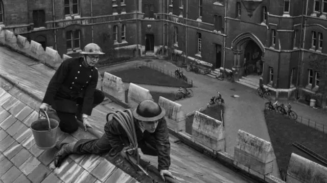 Black and white image of two students on a roof in ARP uniforms