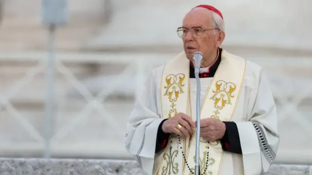 Giovanni Battista Re stands at a microphone in white robes