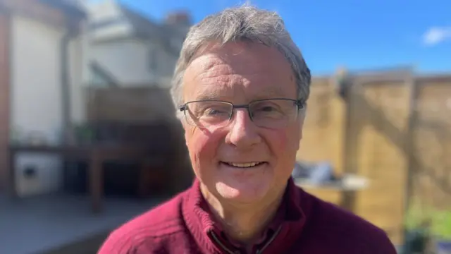 Bill Wright smiles and looks ahead, wearing glasses.