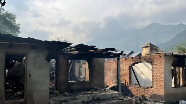 A destroyed building, with smoke billowing in the background