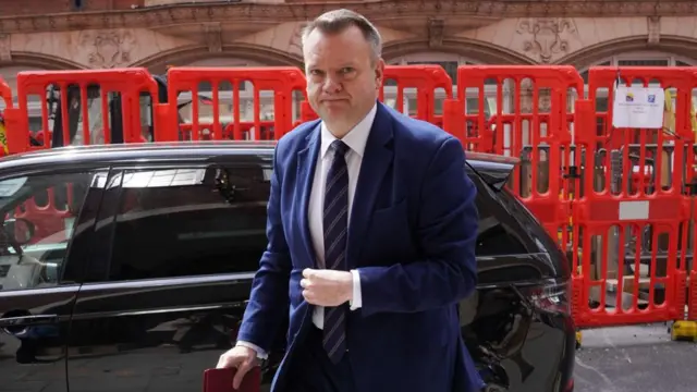 Cabinet Office minister Nick Thomas-Symonds arrives at the Infected Blood Inquiry at Church House, in Westminster, London, wearing a suit and standing in front of a black car.