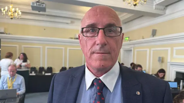 Nigel Hamilton wears a suit and tie with glasses.