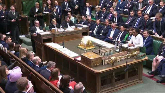 Badenoch asks questions across the dispatch box in the Commons, while Starmer, with his back to camera, sits and listens. The benches are filled with seated MPs