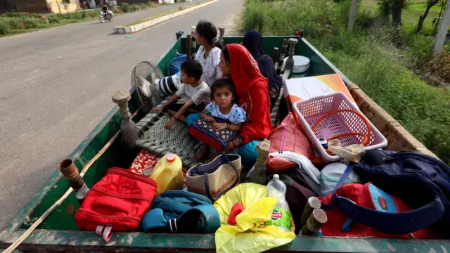 Villagers sit in tractor trolley with their belongings as they move near Suchetgarh