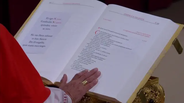 A cardinal's hand, resting on the page where the oath is written