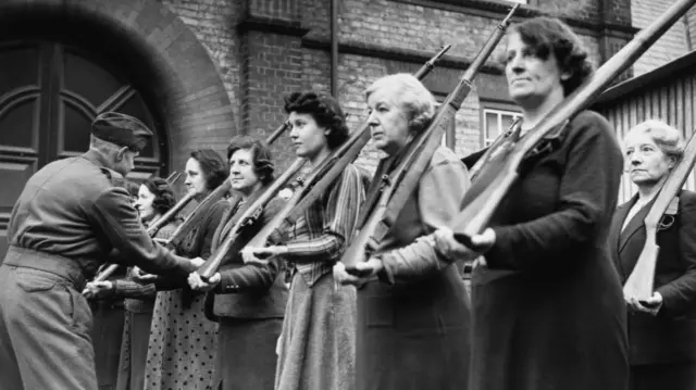 Black and white image of a line of women holding rifles on their shoulders
