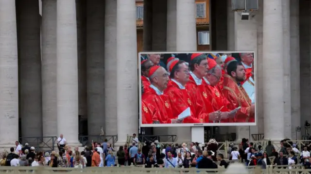People watch a Holy Mass on a large screen in Saint Peter's Square in the Vatican on the first day of the conclave to elect the next pope