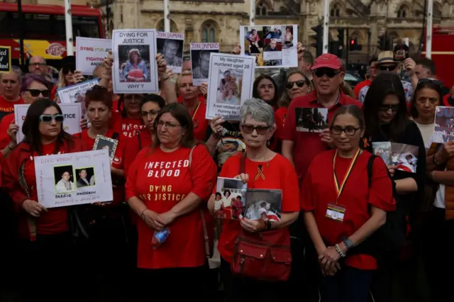People impacted by the contaminated blood scandal gather in Westminster for a vigil to remember those that lost their lives. They all wear red and signs with pictures of victims reading: "Dying for justice".