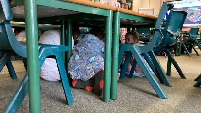 Children in pyjamas seek cover under their school desks during a pretend air raid
