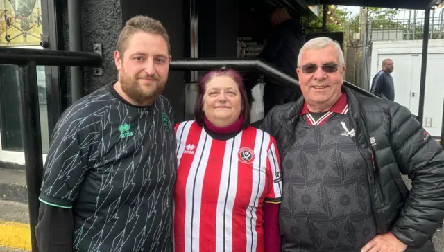 Two men wearing black standing either side of a woman wearing a red and white striped jersey.