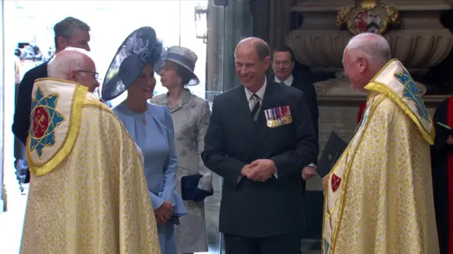 Duchess of Edinburgh in blue dress smiles as she greets clergy next to the Duke of Edinburgh in a suit