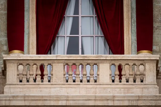 The balcony at the Vatican is seen empty with red curtains covering the glass doors