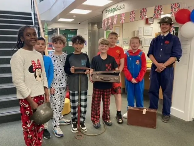 School children standing in a reception area wearing pyjamas.