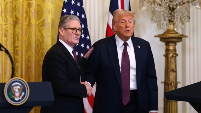 Trump and Starmer shake hands at the White House during a press conference. Both are wearing suits.