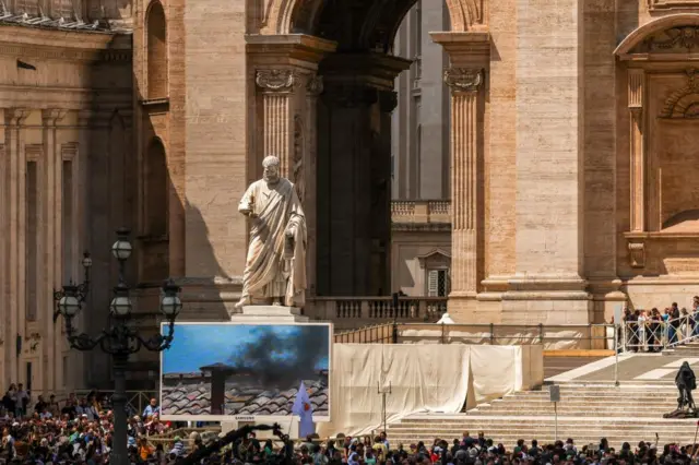 People watch as a screen in St Peter's square shows black smoke rising from the chimney on the Sistine Chapel