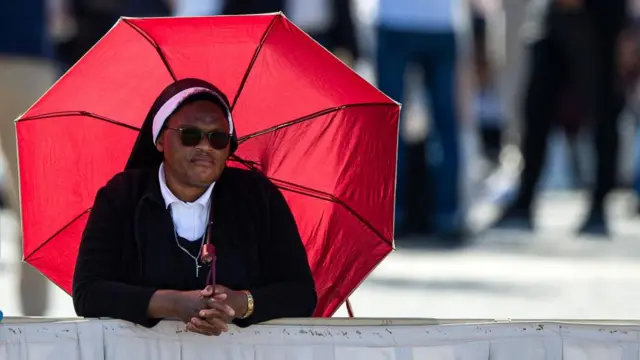 A nun using a red umbrella as a parasol