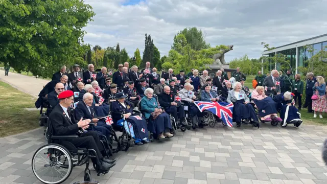 a group of veterans, most of the front row in wheelchairs, pose for a picture at the national memorial arboretum in staffordshire