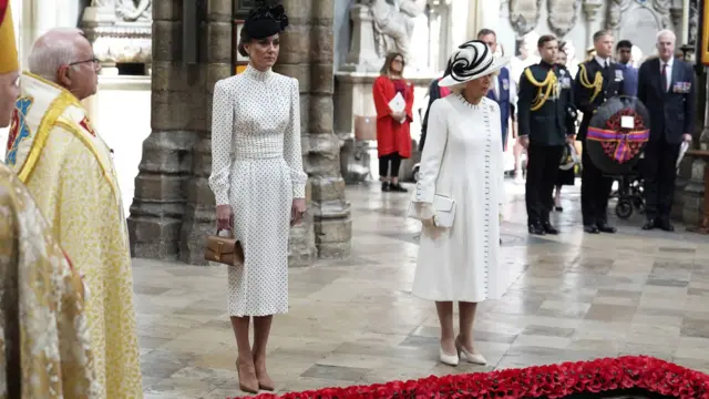 Catherine, Princess of Wales and Queen Camilla both wear white as they bow their heads in silence with other attendees behind them inside the abbey