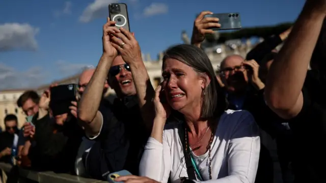 A woman has tears in her eyes and people around her hold up their phones to take pictures