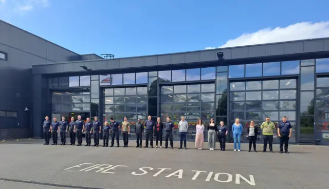 Hampshire and Isle of Wight Fire and Rescue Service staff standing in a line outside a fire station, with engines visible behind glass doors