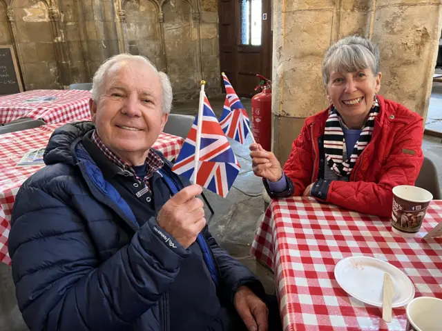 Barry Volans pictured with his wife Gillian. Both are waving small union flags and sitting at a table