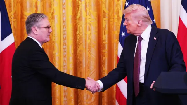 Starmer wears a suit and shakes hands with Donald Trump in the Oval Office, who is also wearing a suit.