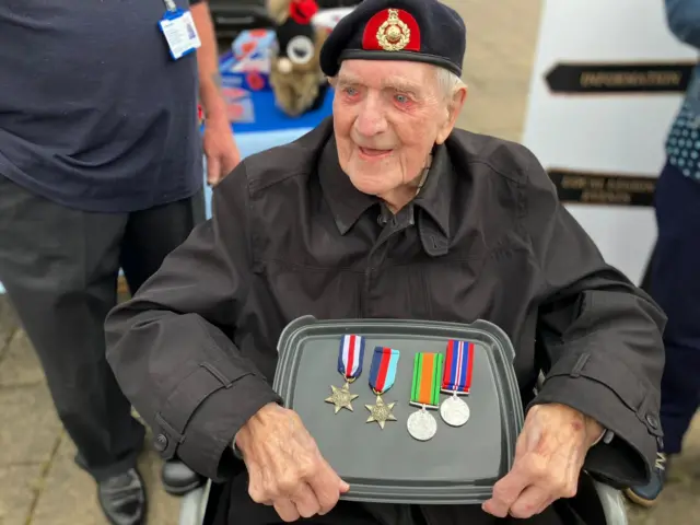 Jim, a 99-year-old Royal Marine veteran from Hessle, is presented with four medals. He is wearing a black overcoat and a black and red beret with a gold badge.