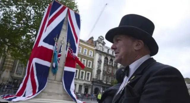 A man dressed in a black suit with bow tie and black hat walks past the Cenotaph in London