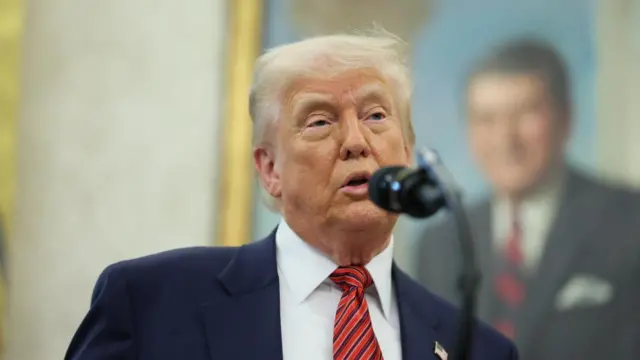 Donald Trump speaks at the White House wearing a suit and red tie, behind a podium with a microphone.