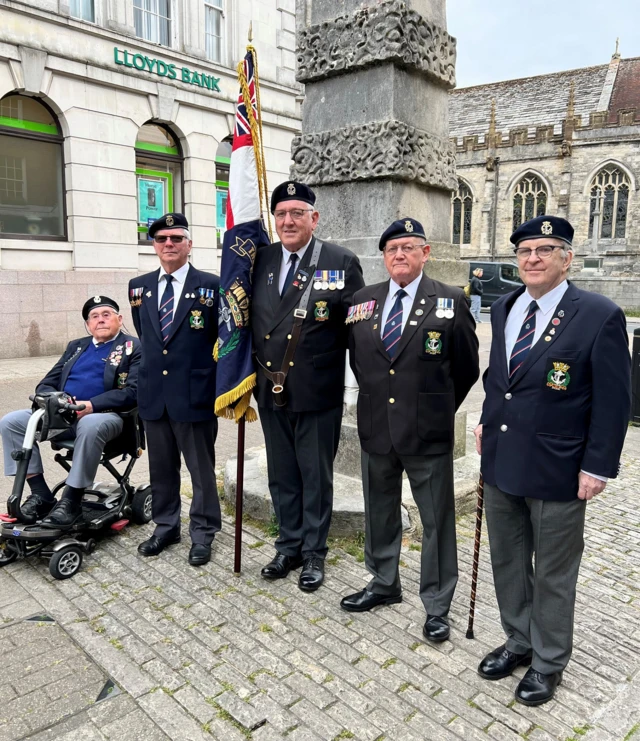 Five members of the Royal Navy Association stood or sat in a mobility scooter in front of Dorchester's war memorial.