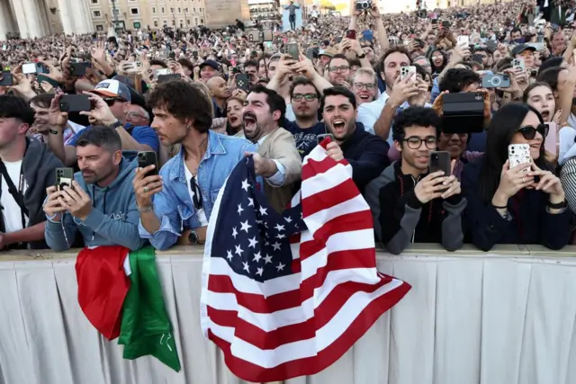 Crowds cheer and one person holds up the American flag