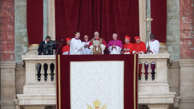 The new pope reads from a sheet of paper. He shares the balcony with a few other cardinals