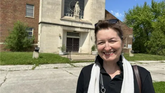 A woman stands smiling outside St Mary of the Assumption, where Pope Leo XIV was a young parishioner
