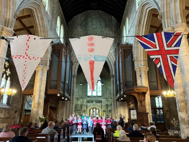 The interior of a church with children on a platform singing - they are wearing uniform and holding song sheets