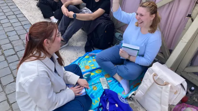 Two women sit and talk while on the ground of St Peter's Square